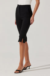 A person is wearing high-waisted black cropped pants with a small slit at the hem on each leg. The pants have a tailored fit with a waistband and belt loops. They are paired with an off-white or cream-colored blouse and black open-toe high-heeled sandals.